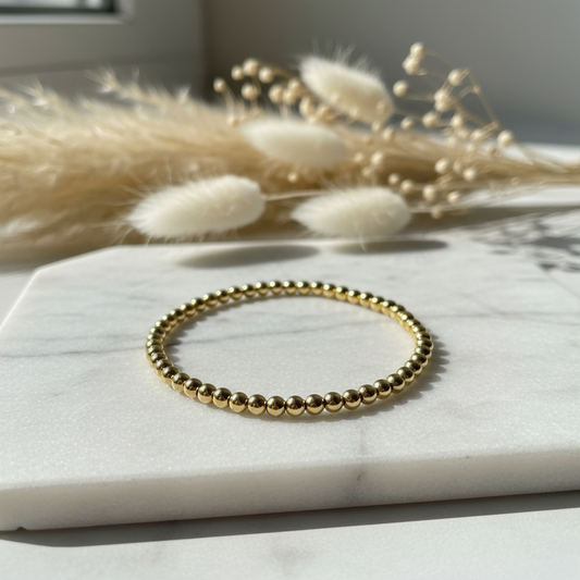 Gold beaded stretch bracelet on white marble surface