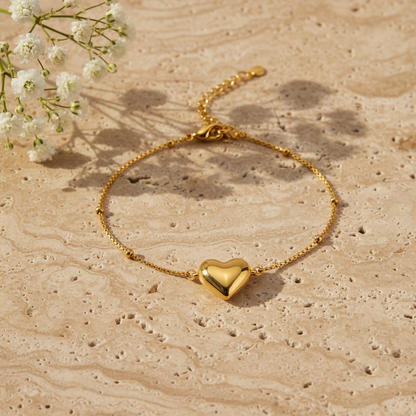 Dainty gold heart charm bracelet on warm stone with flowers