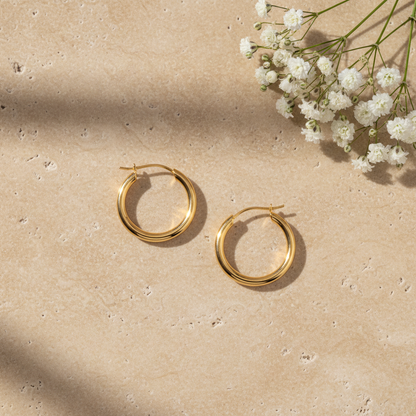 Classic gold hoop earrings on warm stone surface with flowers