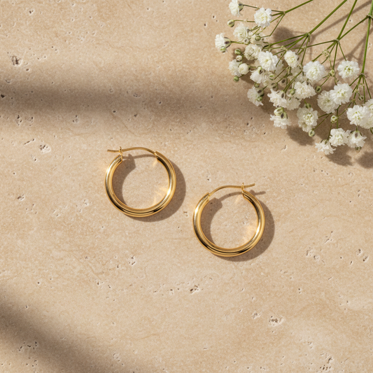 Classic gold hoop earrings on warm stone surface with flowers