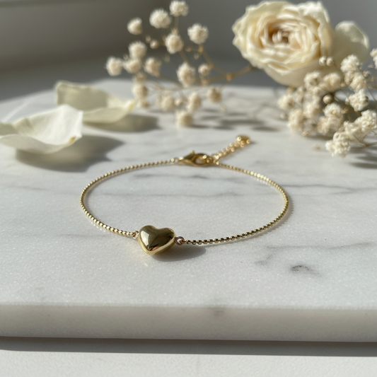 Dainty gold heart charm bracelet on white marble surface