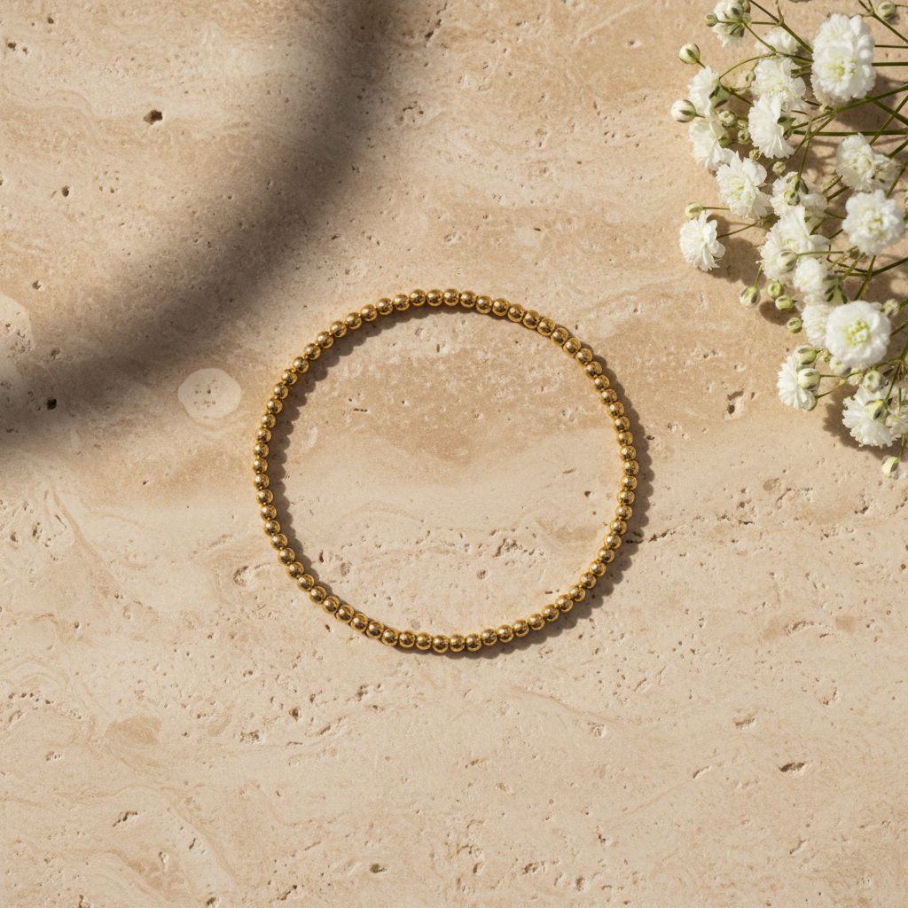 Gold beaded stretch bracelet on warm stone with flowers