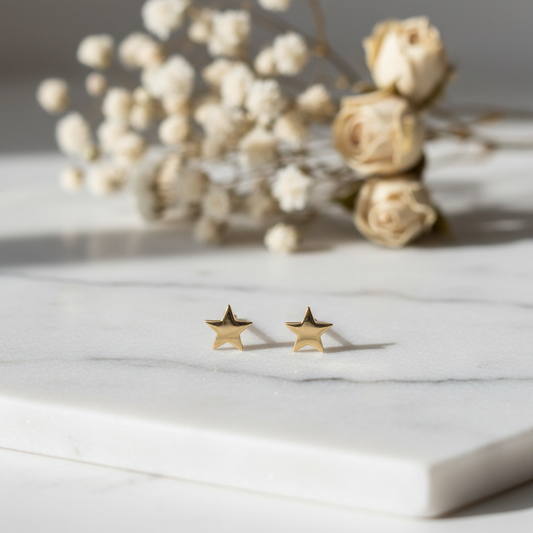 Delicate gold star stud earrings on white marble surface