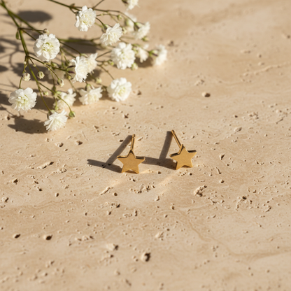 Delicate gold star stud earrings on warm stone with flowers