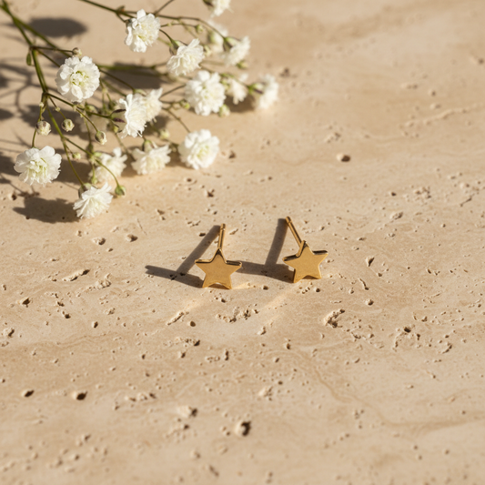 Delicate gold star stud earrings on warm stone with flowers